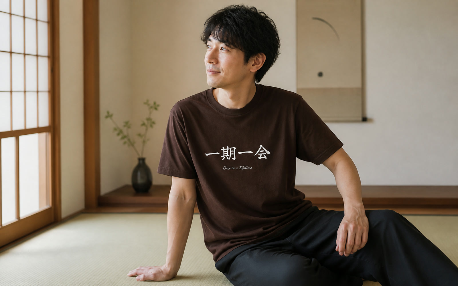 四字熟語Tシャツを着た人物が書道作品の前に立つ写真