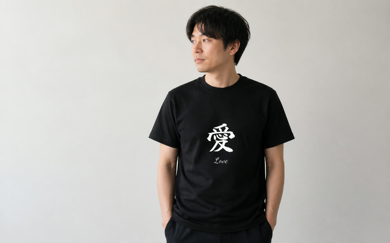 白壁の前で一文字の大判プリントTシャツを着た人物のミニマルなポートレート(字形が主役)